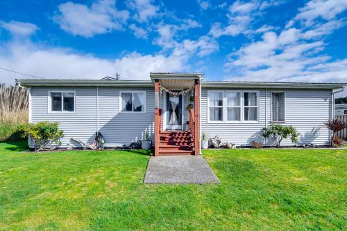 a white house with a red door in a yard at Cozy PNW Getaway with Fire Pit Walk to Beach! in Moclips