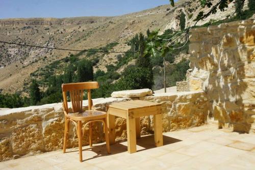 a wooden table and chair sitting next to a stone wall at Dana Hotel in Tufailah