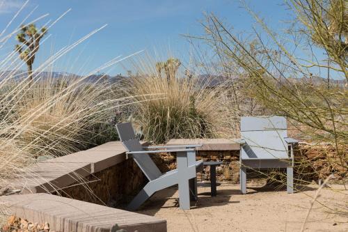 a bench and two chairs sitting in the sand at Joshua Tree Modern Cabin- Goat Mountain Rising in Landers