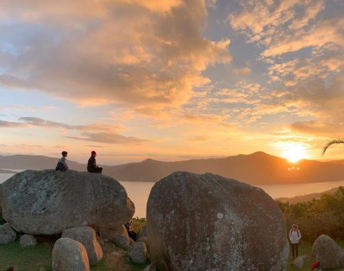 two people sitting on top of a rock at sunset at Nômades Beach - Adventure Hostels in Florianópolis