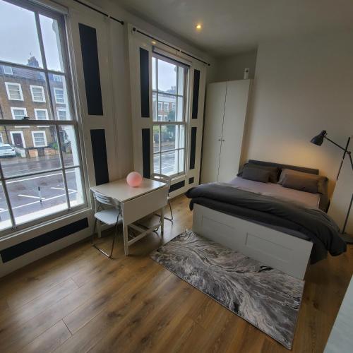 um quarto com uma cama, uma mesa e janelas em London Oasis Studio Apartment em Londres