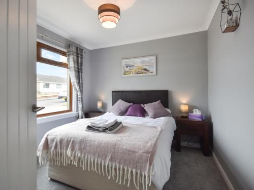 a bedroom with a bed with purple pillows and a window at Fircroft in Glencarse