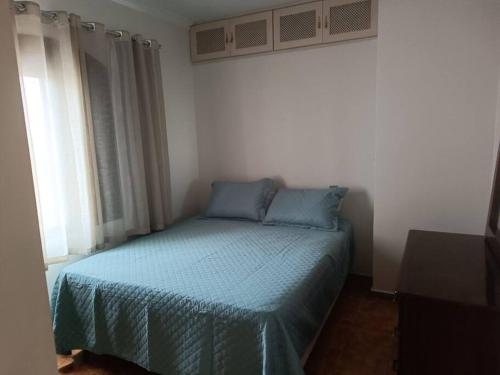 een slaapkamer met een bed met blauwe lakens en een raam bij Apartamento Guarujá Pitangueiras in Guarujá