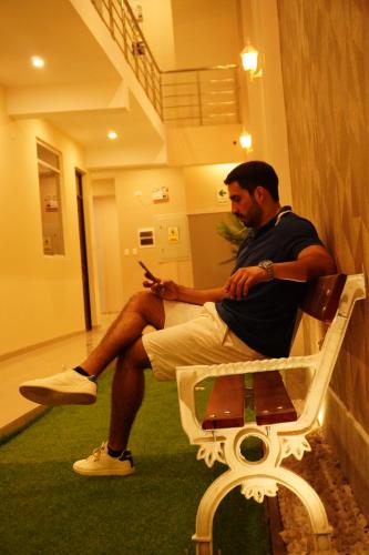 a man sitting on a bench looking at his cell phone at Mak Suites in Piura