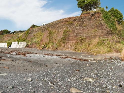 a rocky beach with a hill with trees on it at Ty Mor- Uk46410 in Downderry