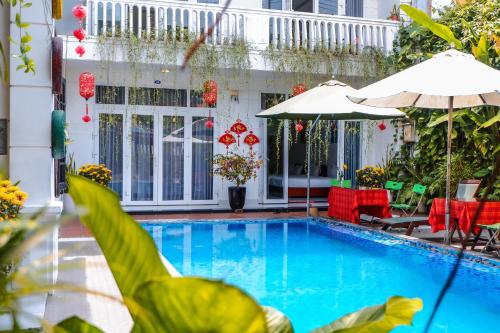 a pool with red chairs and umbrellas next to a building at Oleander Garden Homestay in Hoi An