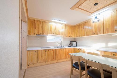 una cocina con armarios de madera, mesa y sillas en 나무집 게스트하우스 en Jeju