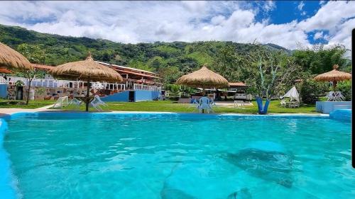 a swimming pool with blue water and straw umbrellas at Cabaña del lago in Cocorná