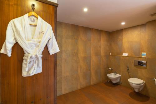 a bathroom with a toilet and a robe hanging on a door at Adamo The Bellus Calangute in Calangute