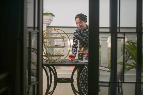 a woman standing at a table with a glass of wine at The Oriental Jade Hotel in Hanoi