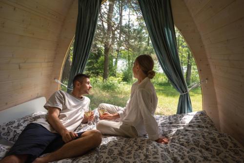 Un uomo e una donna seduti su un letto in una tenda di Miško Maudynės a Kaltanėnai