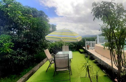 un patio con mesa, sillas y sombrilla en Le gîte du pavé, en Saint-Paul