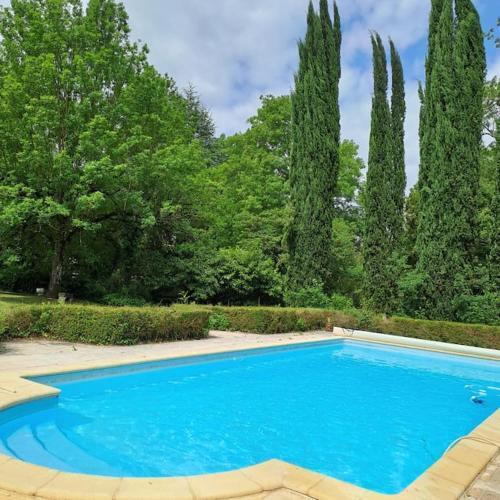 une piscine bleue dans un jardin arboré dans l'établissement Gîte Le Pavillon dans le parc du Château Lescaut, à Montignac-de-Lauzun