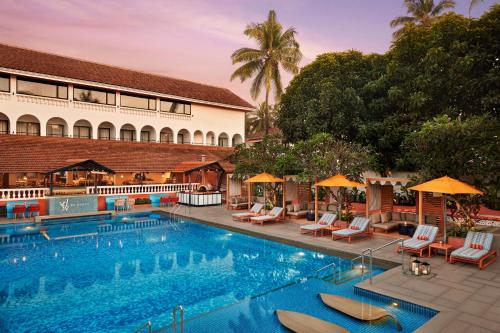 カラングートにあるRonil Goa - a JdV by Hyatt Hotelの建物の隣にスイミングプール(椅子、パラソル付)