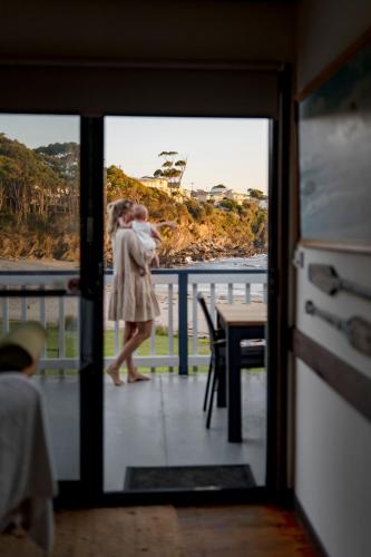 a woman walking on a balcony with a view of the ocean at Beachfront Shack Malua Bay - Dog Friendly with EV Fast Chgr in Malua Bay