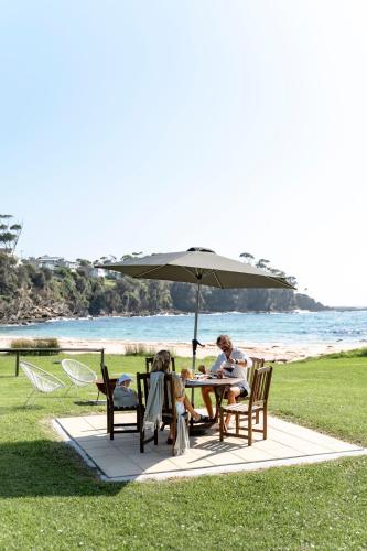 two people sitting at a table under an umbrella at Beachfront Shack Malua Bay - Dog Friendly with EV Fast Chgr in Malua Bay