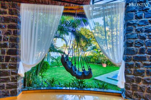 a hammock hanging from a window with a garden at EKO STAY - The Ranch Villa in Deolāli