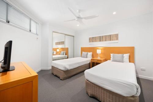 Cette chambre comprend deux lits et une télévision. dans l'établissement Amazing Water View Apartment - Pool, Gym, Parking., à Urangan