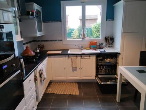 une cuisine avec des armoires blanches, un évier et une fenêtre dans l'établissement Maison 6 pers. à 45 min de Paris, à Ballancourt