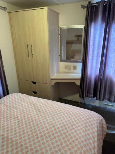a room with a bed and a cabinet with a mirror at 3 BEDROOM CARAVAN AT THE GRANGE HOLIDAY PARK, CHAPEL ROAD INGOLDMELLS in Addlethorpe
