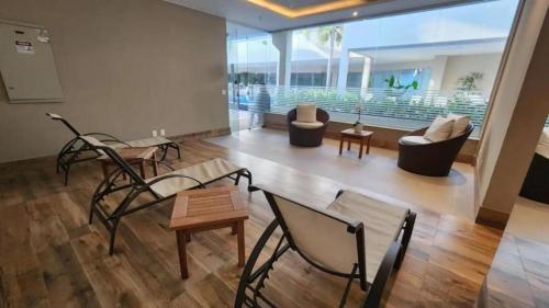 a living room with chairs and tables and a large window at Apartamento Neolink Barra da Tijuca in Rio de Janeiro