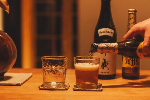 a person pouring a beer into two glasses on a table at Une stay&diner in Sasayama