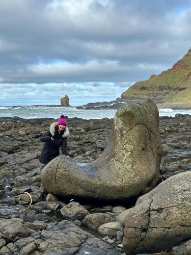 a woman standing next to a large rock on a rocky beach at Braeside B&B in Bushmills
