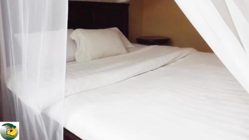 um quarto com uma cama com lençóis brancos e cortinas em Antique Apartments em Entebbe