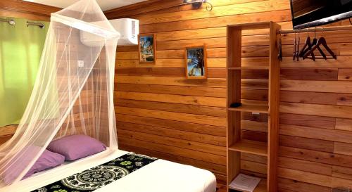 ein Schlafzimmer mit Holzwänden und einem Bett mit einem Vorhang in der Unterkunft Cazadodo in L’Étang-Salé