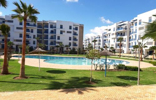 a swimming pool with palm trees and buildings at Appartement de Luxe MARTIL COSTA MAR Pour Familles in Martil