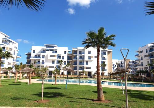 a resort with a pool and palm trees and buildings at Appartement de Luxe MARTIL COSTA MAR Pour Familles in Martil