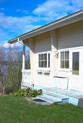 a white house with a wooden porch on a lawn at LAKESIDE COTTAGE Private beach in Ikaalinen