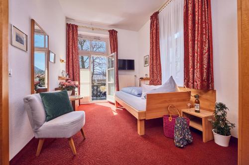 um quarto com uma cama, uma cadeira e uma janela em Hotel Aschenbrenner em Garmisch-Partenkirchen