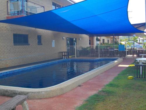 uma piscina com um guarda-sol azul ao lado de um edifício em Kurrimine Beach Motel em Kurrimine Beach