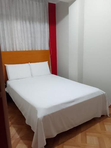 a white bed in a room with a red wall at Hostal Terraoro in Lambayeque