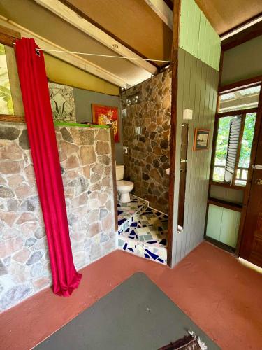 a bathroom with a toilet and a stone wall at Cocoa Cottage in Roseau