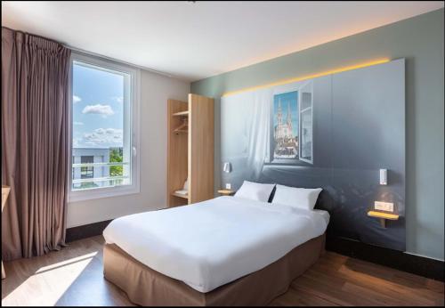ein großes weißes Bett in einem Zimmer mit Fenster in der Unterkunft B&B HOTEL CHARTRES Oceane in Chartres