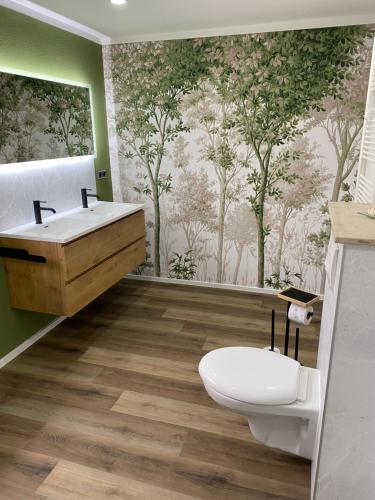een badkamer met een toilet, een wastafel en een muurschildering van bomen bij Ferienwohnung Romantica 1. und 2. OG in Schopfloch