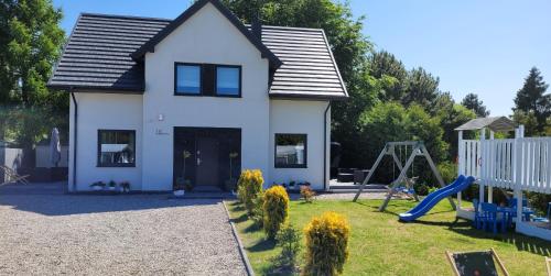 een wit huis met een speeltuin in de tuin bij DĘBKI DOMKI SASANKOWE in Dębki