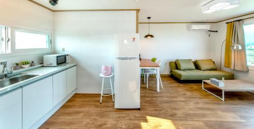 a kitchen with a refrigerator and a table and a couch at Boreum Pension in Seogwipo