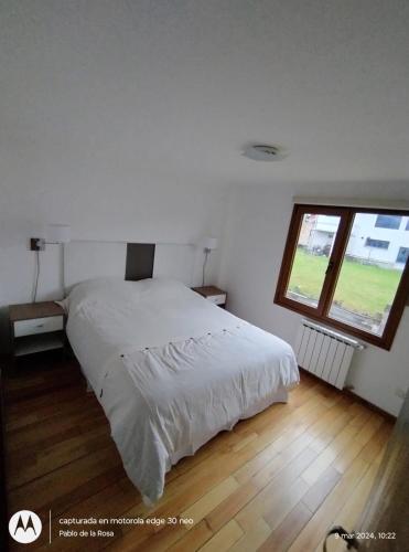 a bedroom with a white bed and a window at Mirando al Sol Ushuaia in Ushuaia
