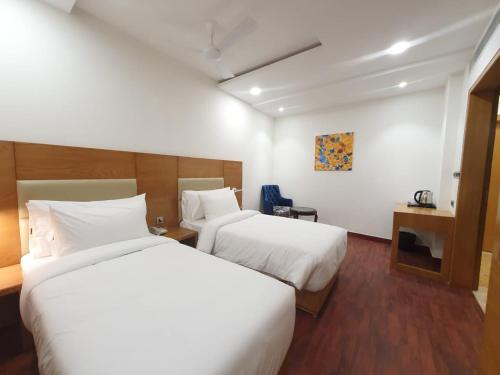 duas camas num quarto de hotel com lençóis brancos em The Moziac Hotel em Gwalior