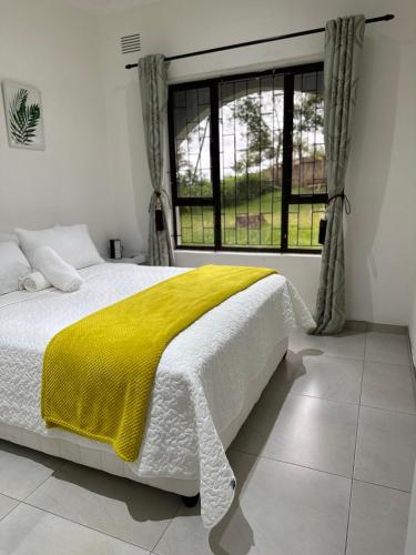 a bedroom with a bed with a yellow blanket and a window at Cliffside Cottage in Kloof