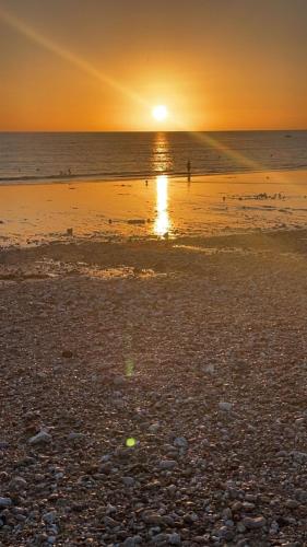 - un coucher de soleil sur une plage avec une personne debout dans l'eau dans l'établissement Bord de mer Le Havre, au Havre