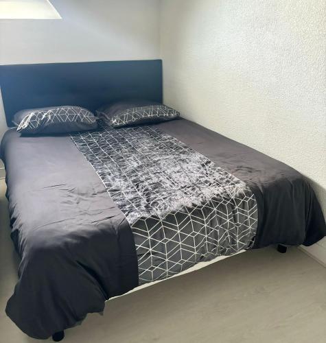 a bed with a black and white comforter and pillows at New Studio Cosy - Proche RER et centre ville in Brétigny-sur-Orge