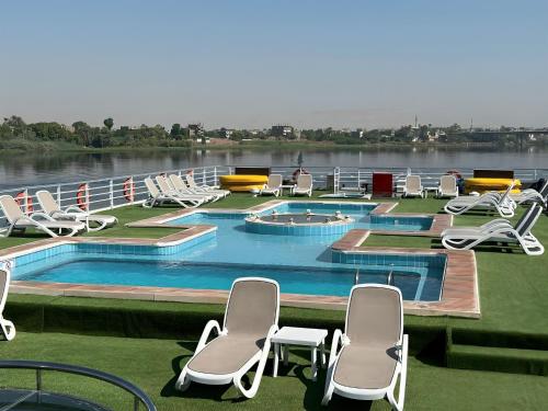 a large swimming pool with chairs and a lake at Nile cruise, Luxor, Aswan, Floating hotel Alhambra A F in Aḑ Ḑab‘īyah