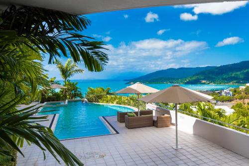 Una piscina con sillas y sombrillas y el océano. en Pacific Blue - Premiere, en Airlie Beach