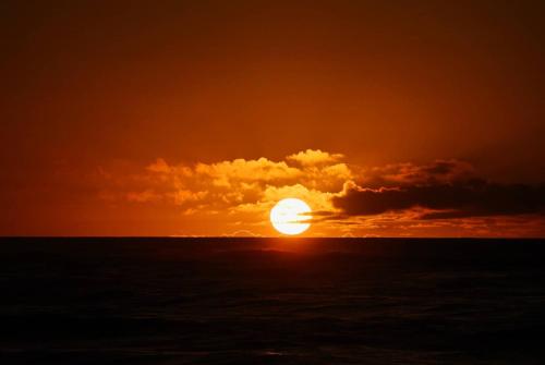 a sunset over the ocean with the sun hiding behind clouds at Kahu's Nest in Hokitika