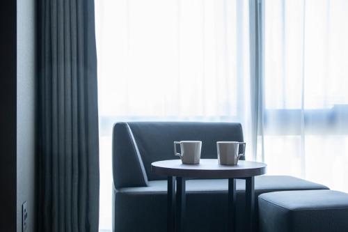 a table in front of a chair with two cups on it at Hotel Keihan Tenmabashi Ekimae in Osaka