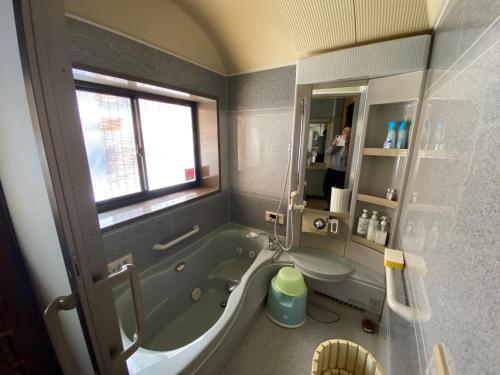 a bathroom with a tub and a person in a mirror at ゲストハウスすまいるさん in Iba